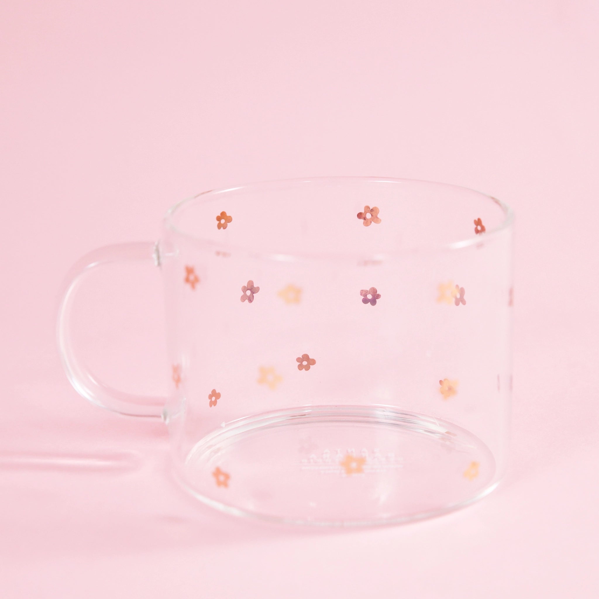 On a light pink background is a clear glass mug with small gold daisy design all over.