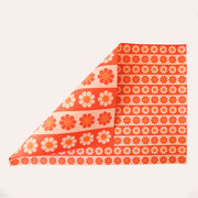 Sheet of wrapping paper filled with stripes of bright and pastel orange flowers. The sheet is bent forward, revealing the other side of the wrapping paper. The back side is covered in larger stripes of the same floral print.  