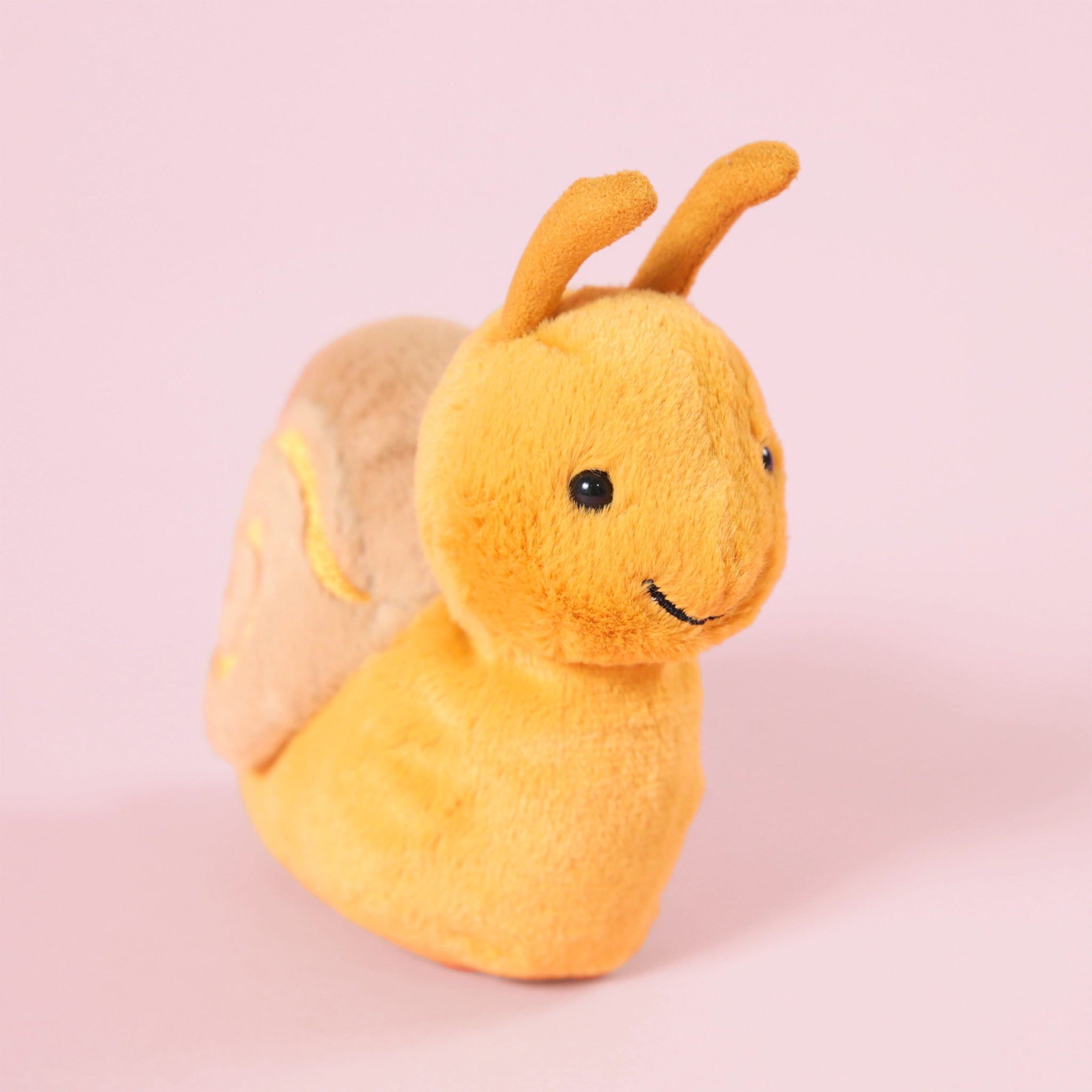A yellow snail stuffed animal with a tan shell and a swirl design in the center and a smiling face.