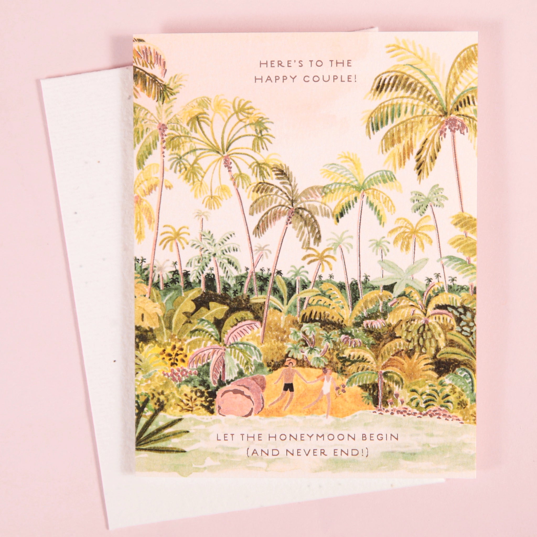 On a light pink background is a white envelope and card with a lush tropical illustration filled with palm trees and a couple holding hands on a beach toward the bottom along with text that reads, "Here's to the happy couple! Let the honeymoon begin (and never end!)".