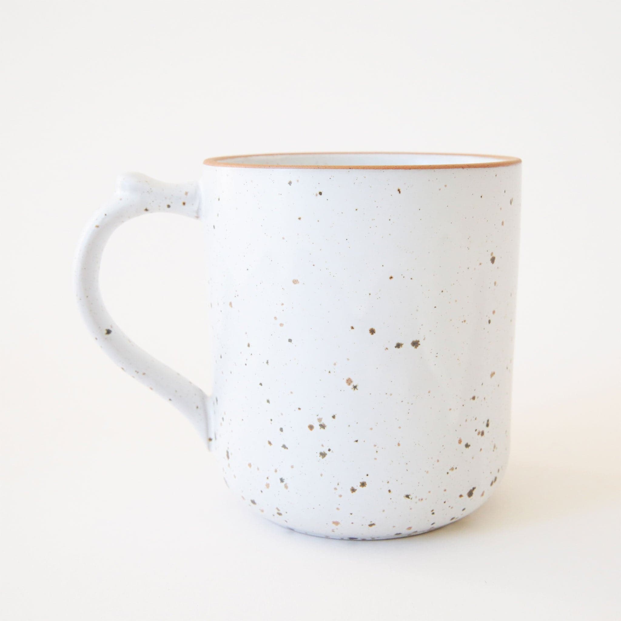 White ceramic mug with brown speckles. The mug has a curved handle with a small notch near the upper half. The top edge of the mug is lined in a caramel brown. 