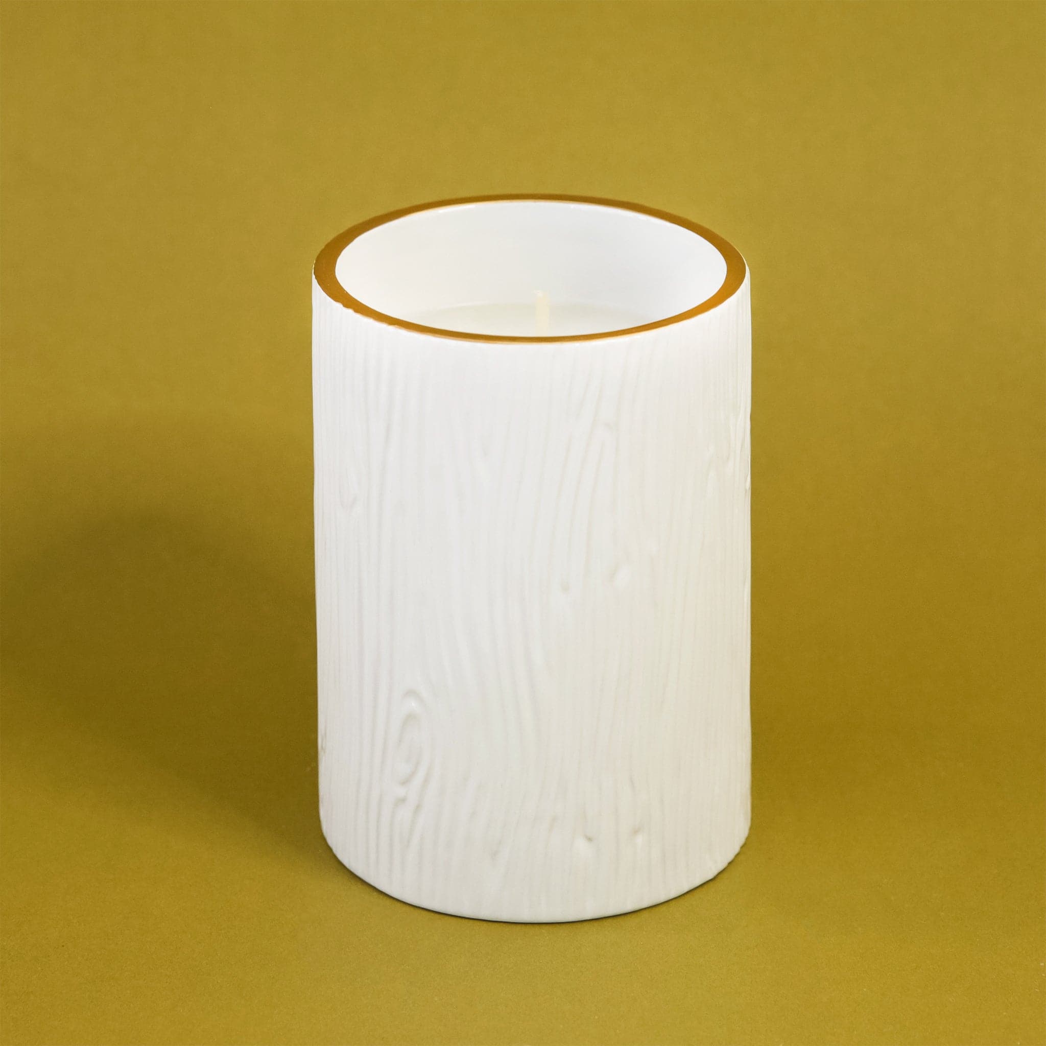 On a green background is a white candle with a wood texture glass.  