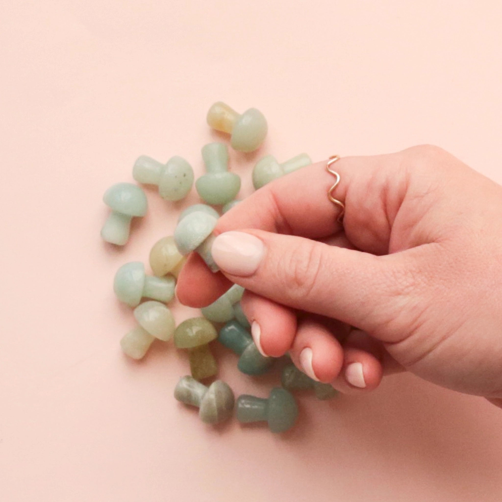 On a pink background is a handful of tiny mushroom shaped Amazonite crystals. 