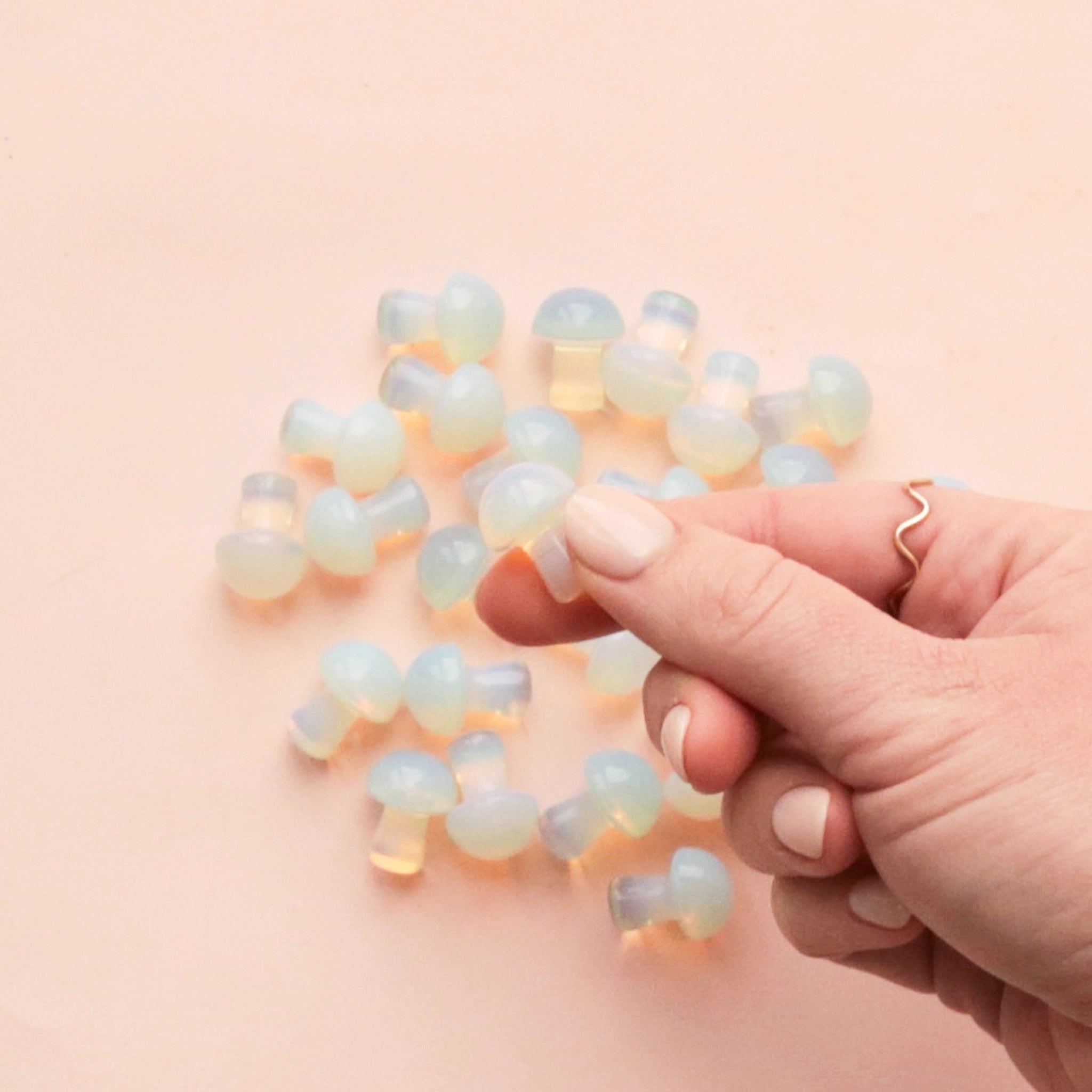 A handful of the tiny mushroom shaped Opal stones on a pink background.