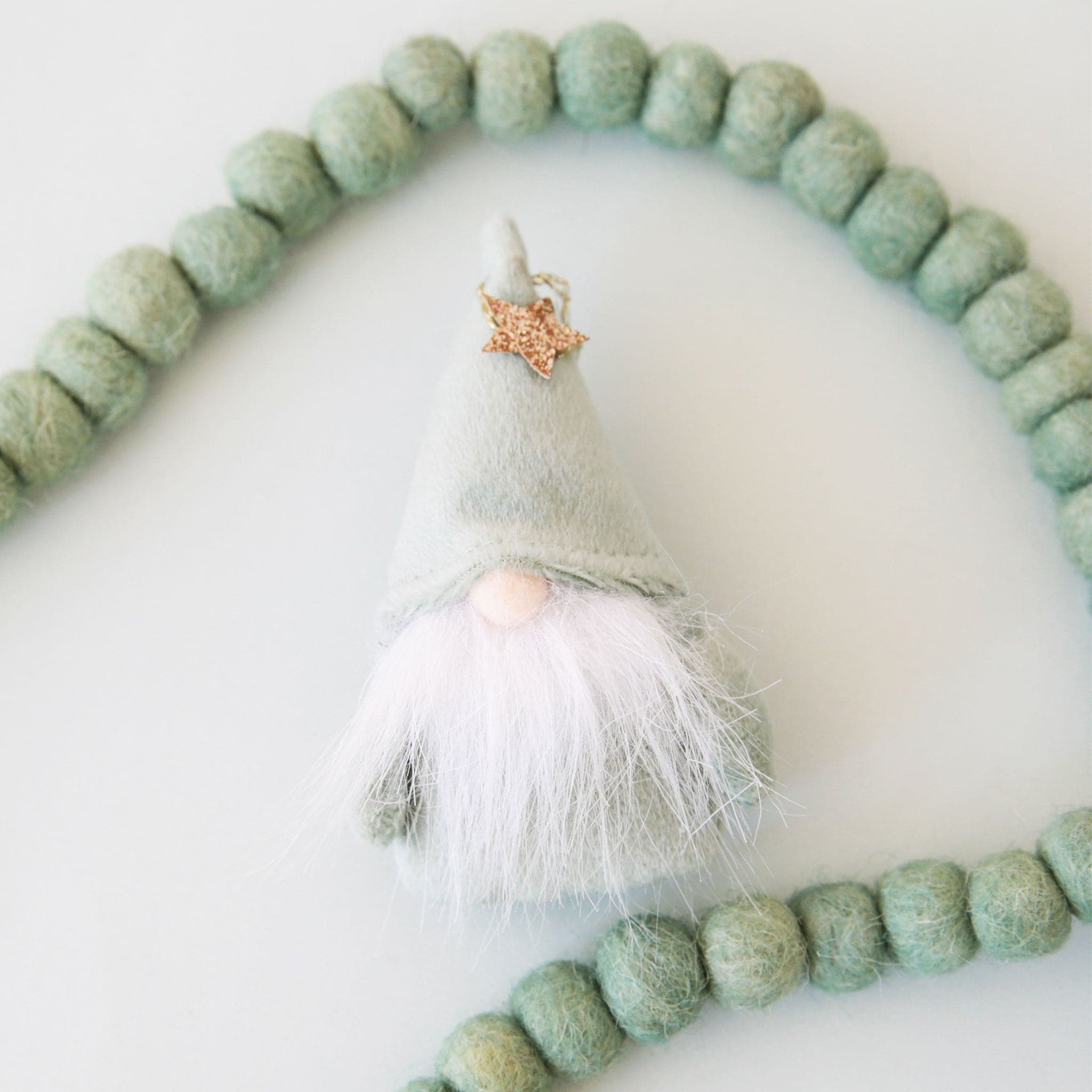 A plush mint green gnome ornament with a gold star and beard on a neutral ground.