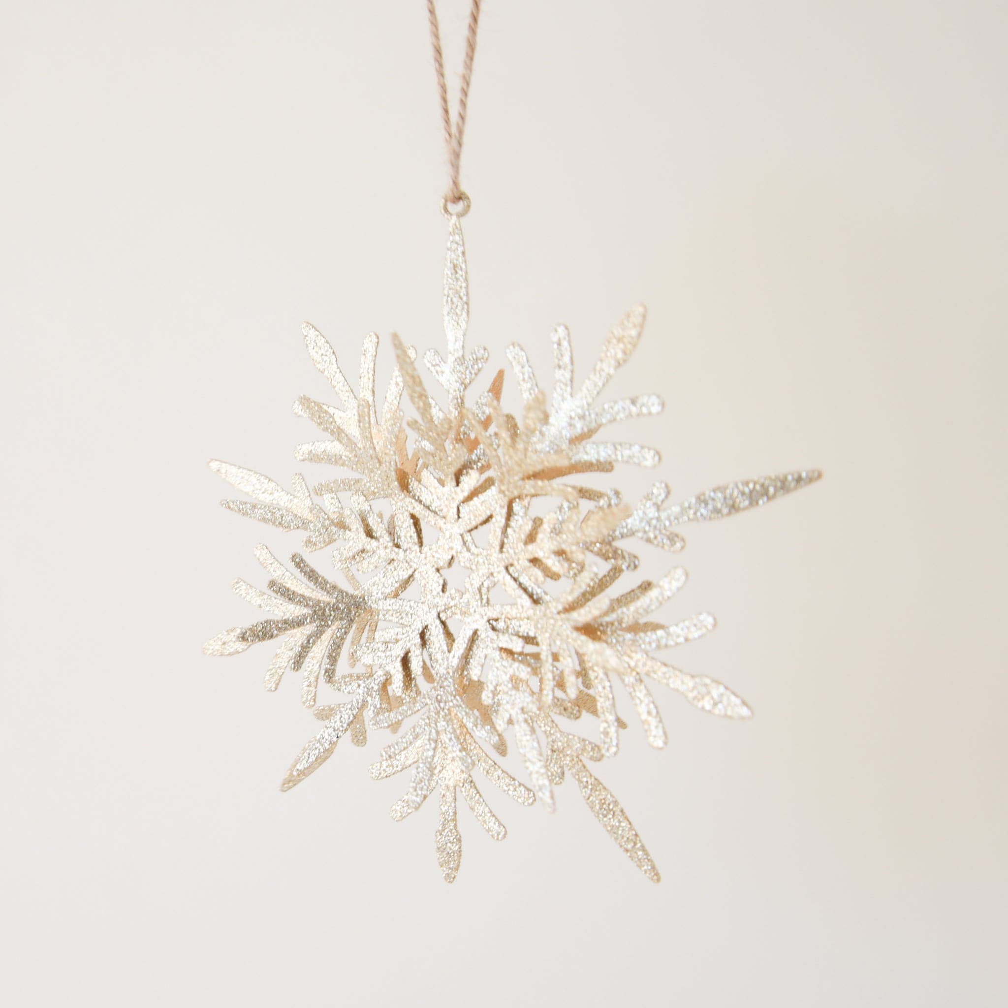 On a neutral background is a gold glitter snowflake ornament.