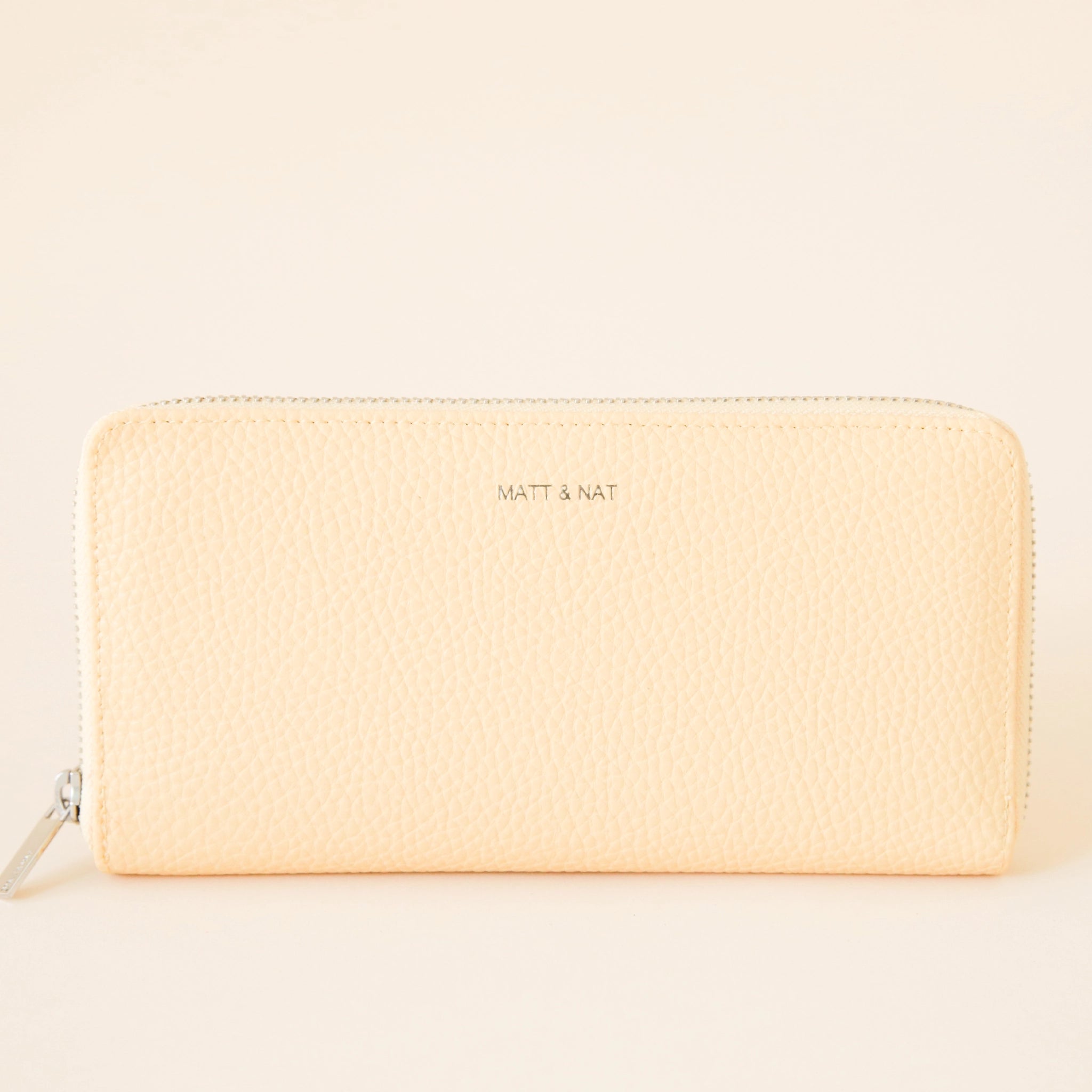 On a cream background is a light yellow zip wallet with silver detailing and "Matt & Nat" written tiny on the front of the wallet. 