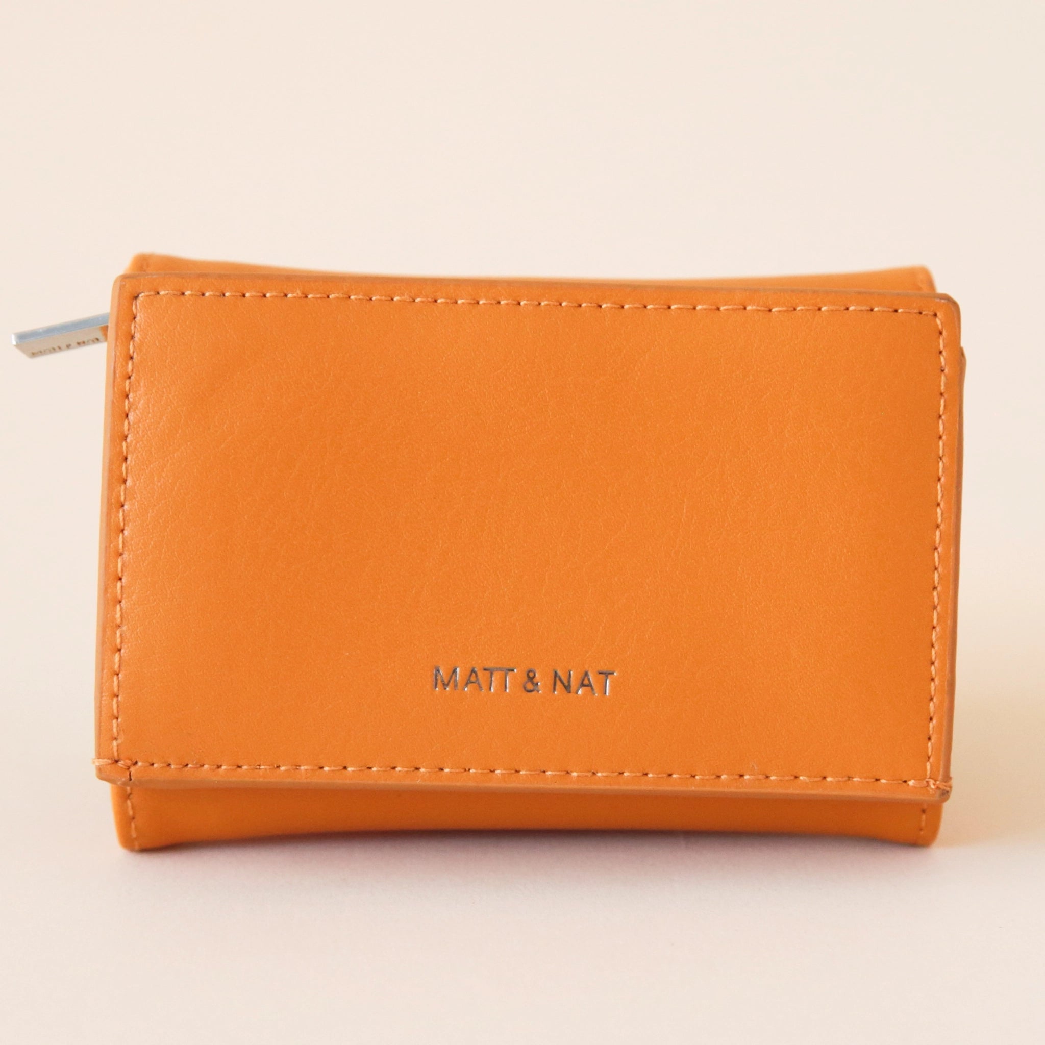 On a cream background is a bright orange colored squares wallet with a folding detail and tiny text on the bottom of the front that reads, "Matt & Nat".