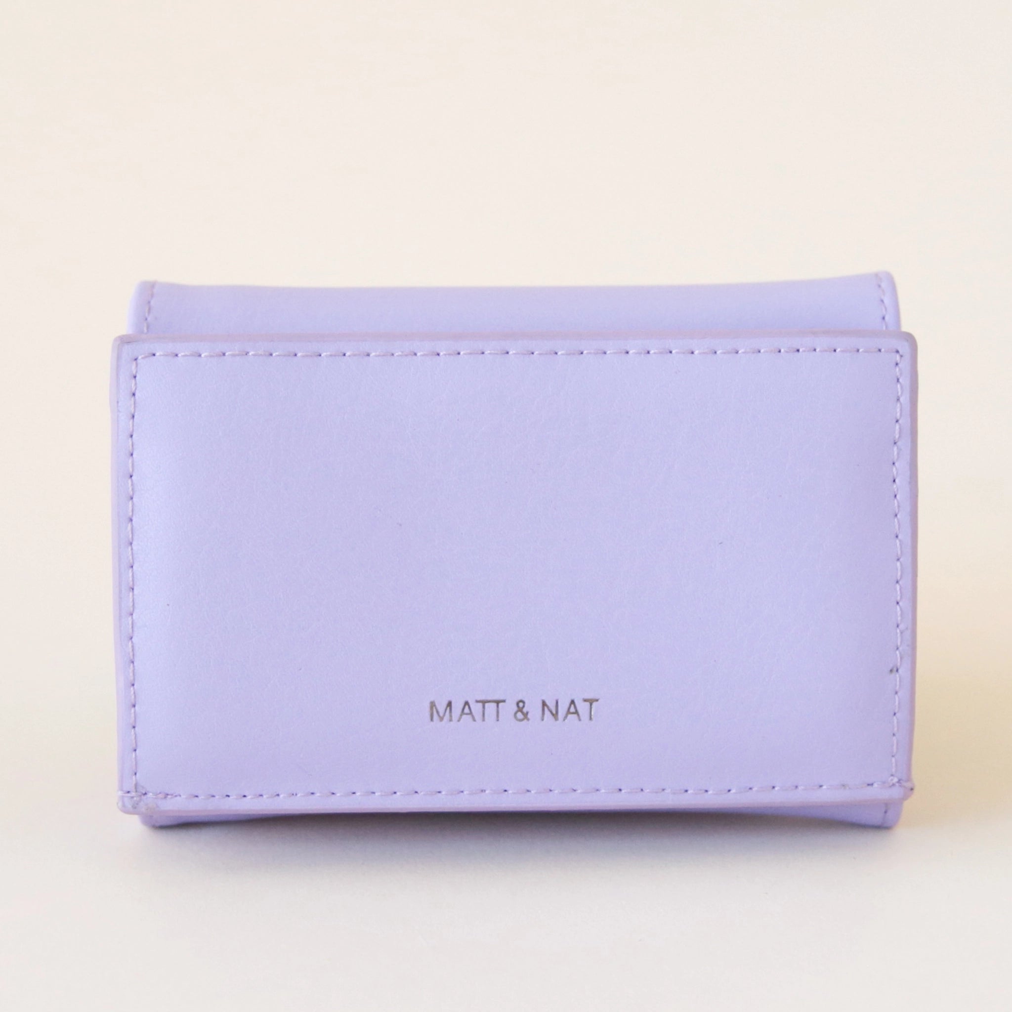 On a cream background is a lavender colored squares wallet with a folding detail and tiny text on the bottom of the front that reads, "Matt & Nat". 