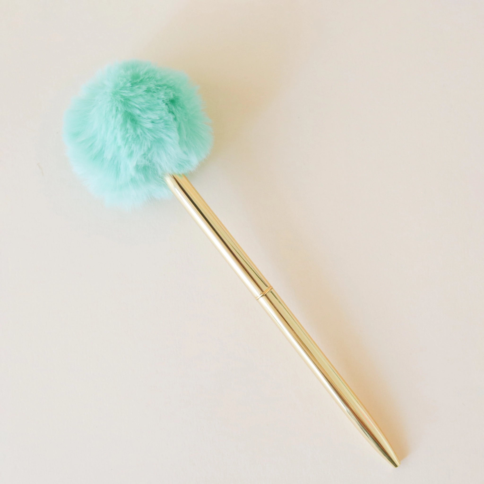 A thin gold pen with a fluffy mint green pom pom at the end.