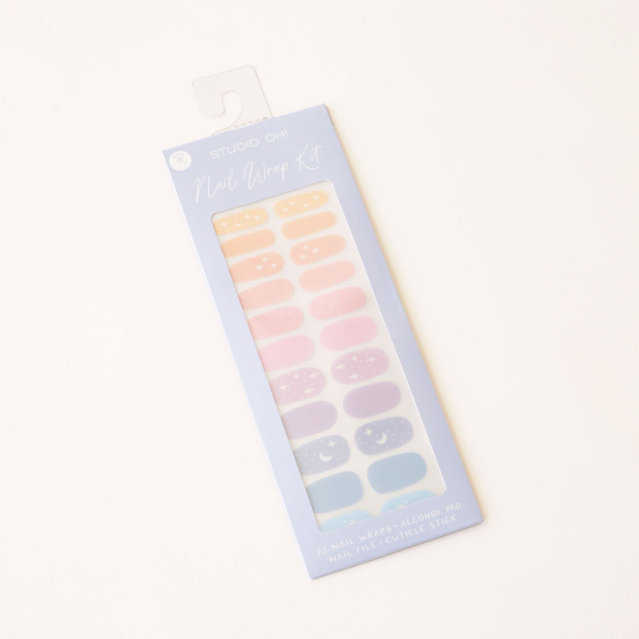 In front of a white background is a lavender rectangular shaped package. There is a clear cut out in the center with pastel nail wraps inside. The wraps are pastel blue, purple, pink and orange. Some have white moons and stars on them. 