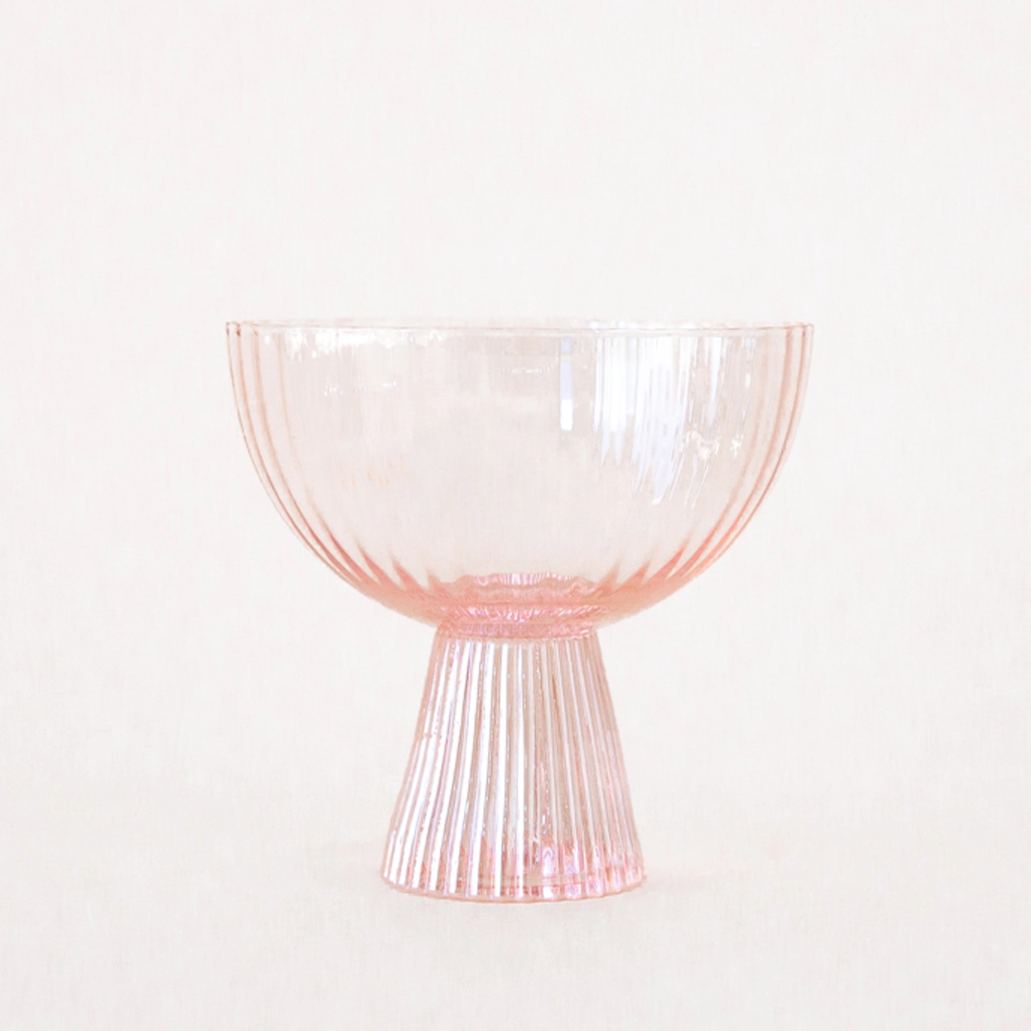 On a white background is a ribbed light pink coupe glass. 