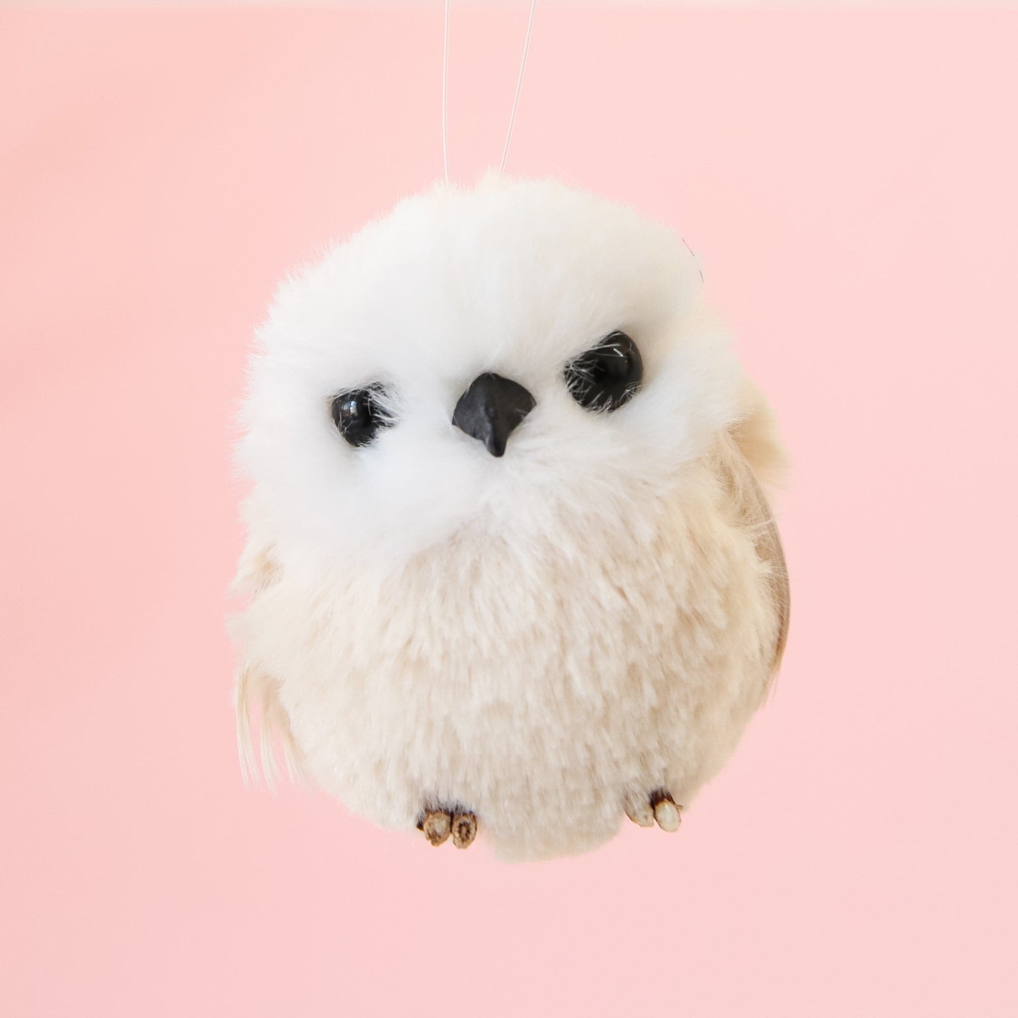 A round baby owl ornament with a black beak and black eyes and a cream colored body.