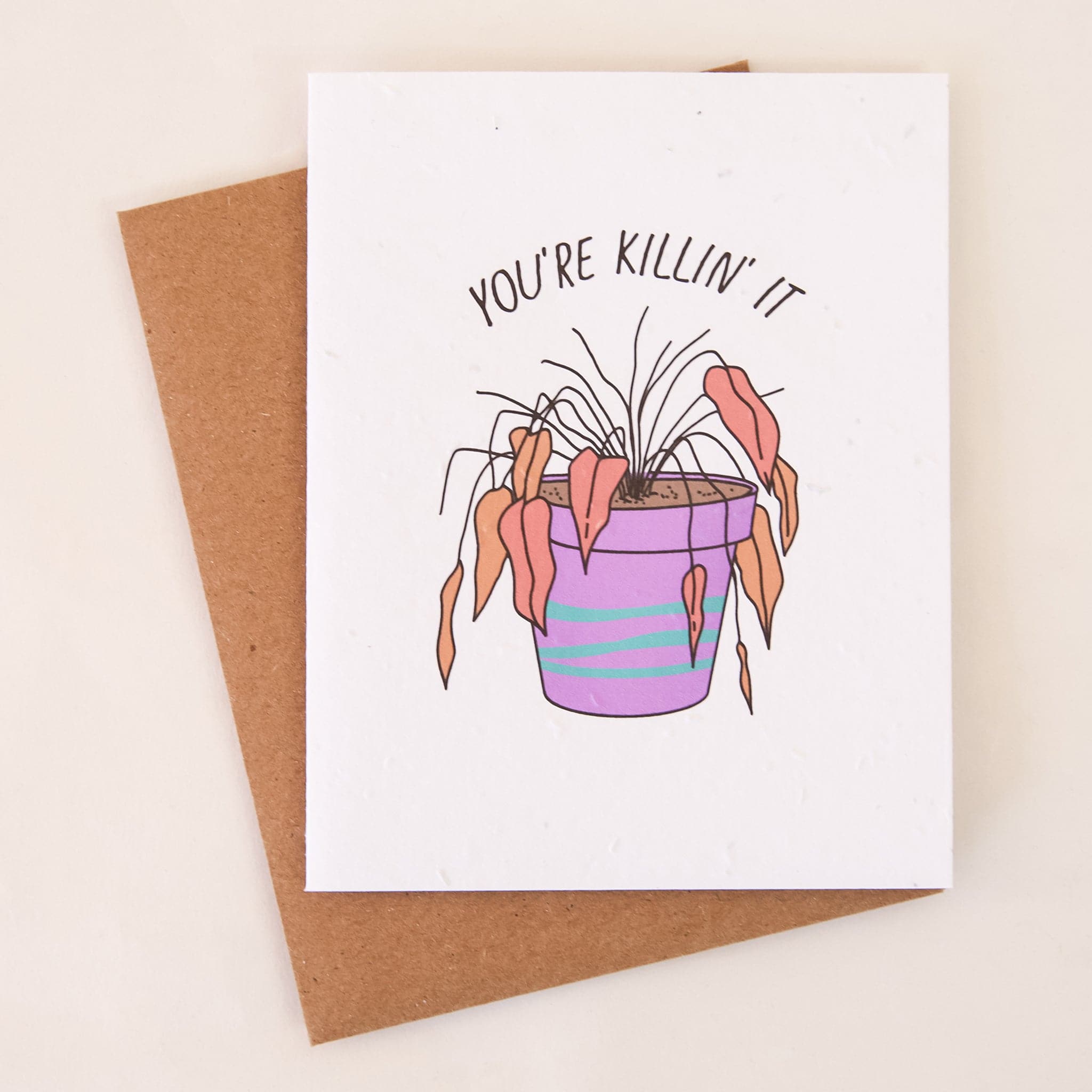 A white card with a illustration of a purple pot with a dead/dying house plant with wilted, drooping leaves and black line letters that read, "You're Killing' It" and also includes a kraft brown envelope.