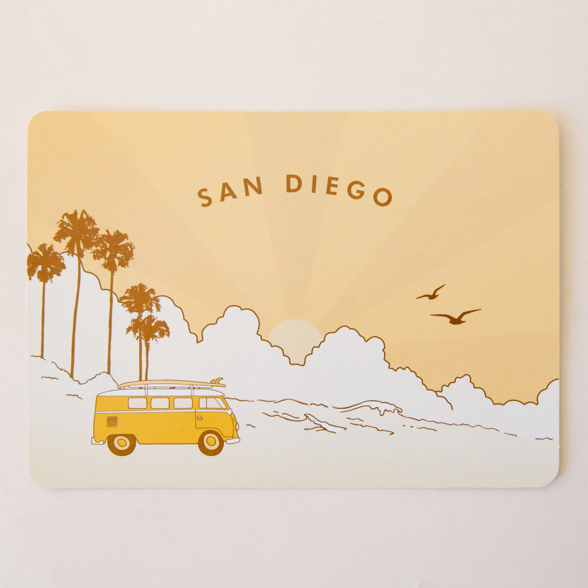 A yellow and cream postcard with a San Diego beach graphic design with palm trees and birds in the background along with a bright yellow VW bus that has a surf board on top as well as text curved along the top that reads, "San Diego".