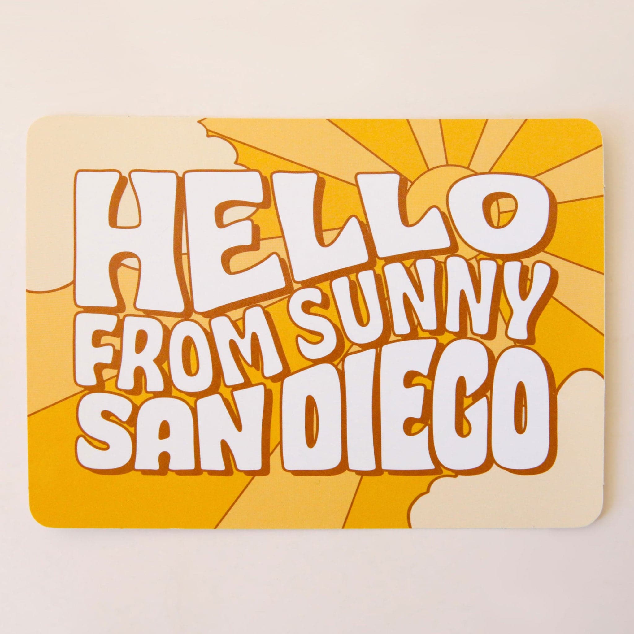 On a cream background is a yellow postcard with a sun and sunray illustration along with text in the center that reads, "Hello From Sunny San Diego" in cream letters. 