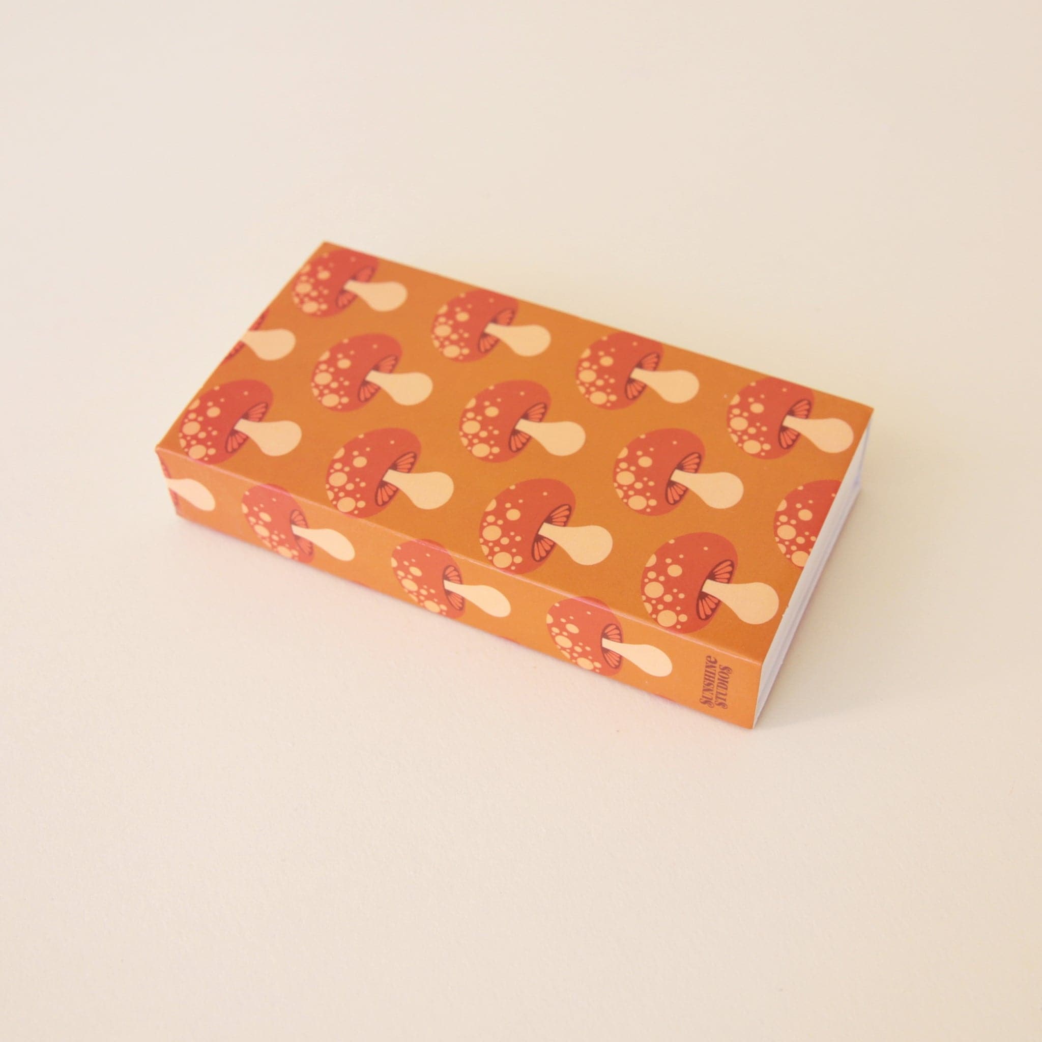 A rectangle box of matches with a repeating red mushroom design along all edges besides the top and bottom.