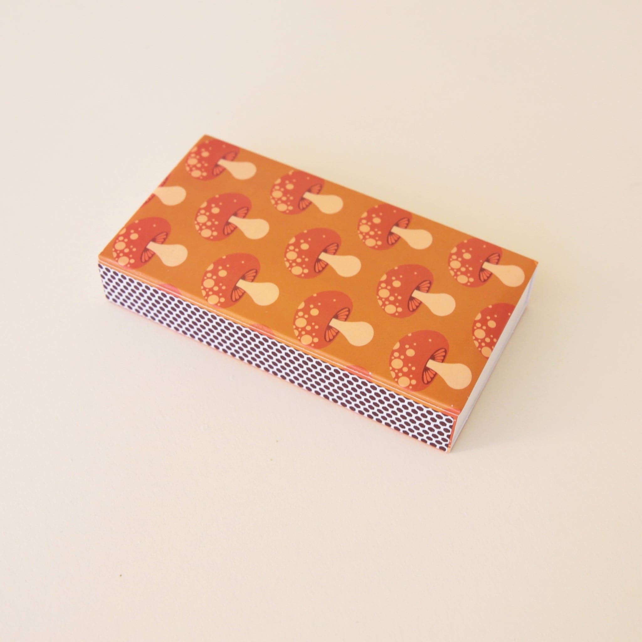 A rectangle box of matches with a repeating red mushroom design along all edges besides the top and bottom.