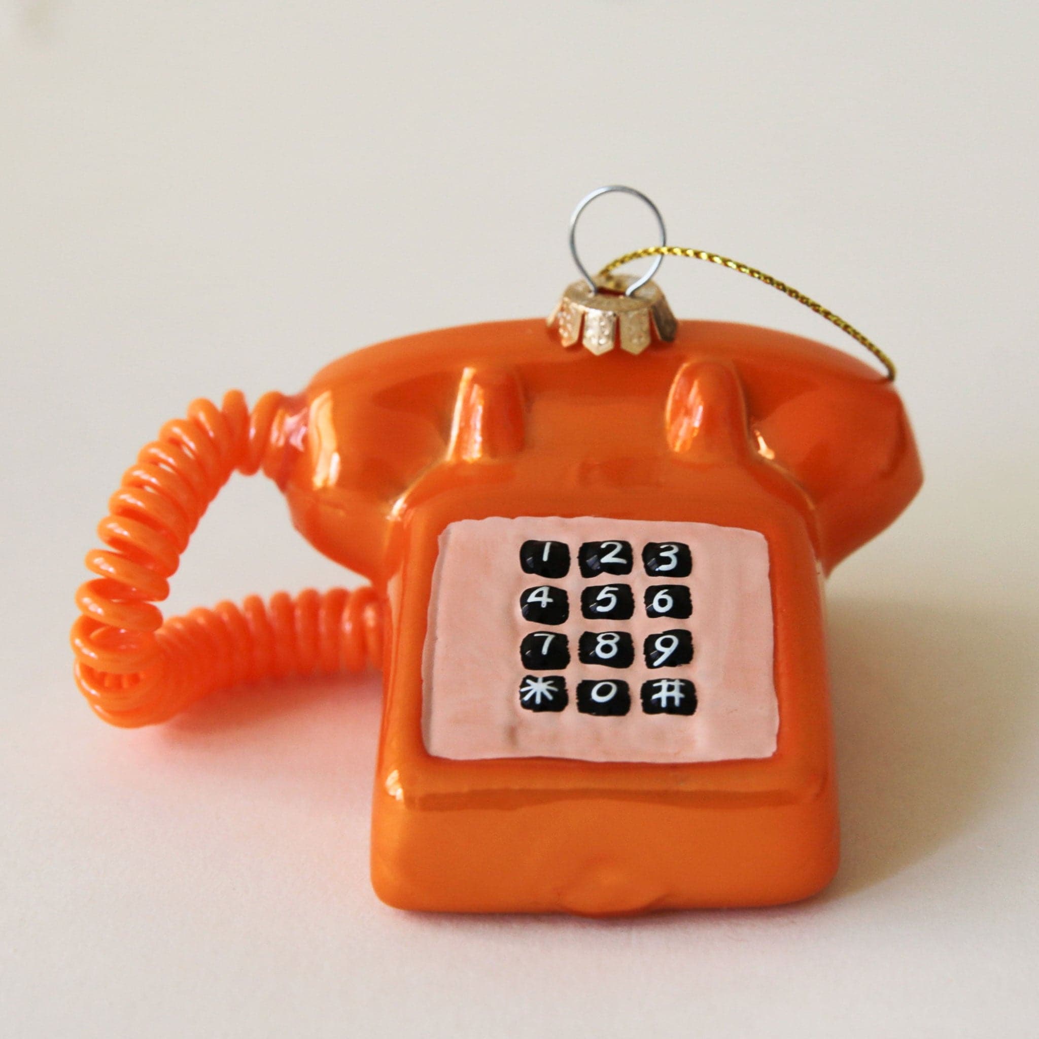 A touch tone phone ornament in a shiny orange color.