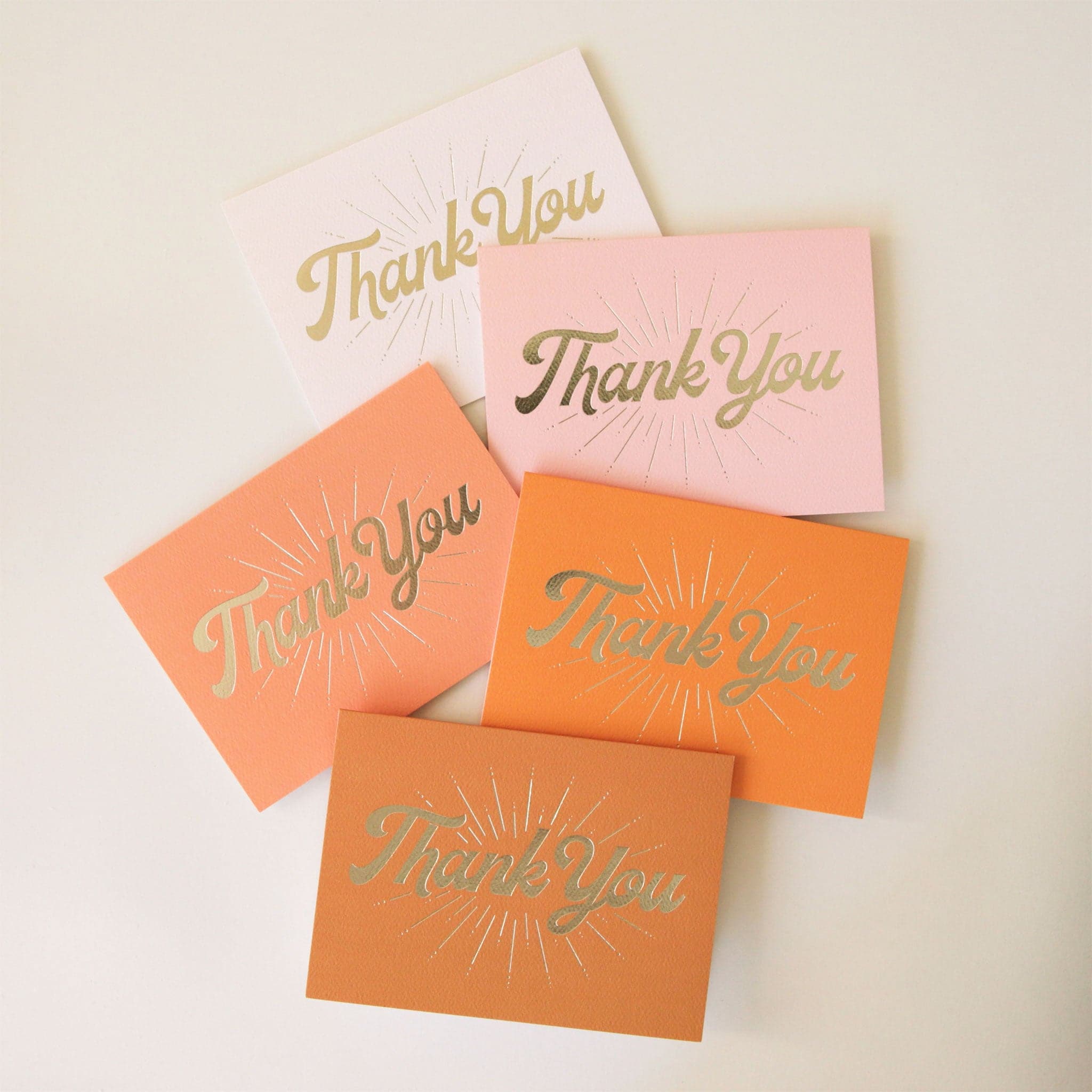 A pack of five different colored folded thank you cards with gold cursive font on the front that reads, &quot;Thank You&quot; along with gold line detailing. The colors range from ivory to light pink to terracotta.