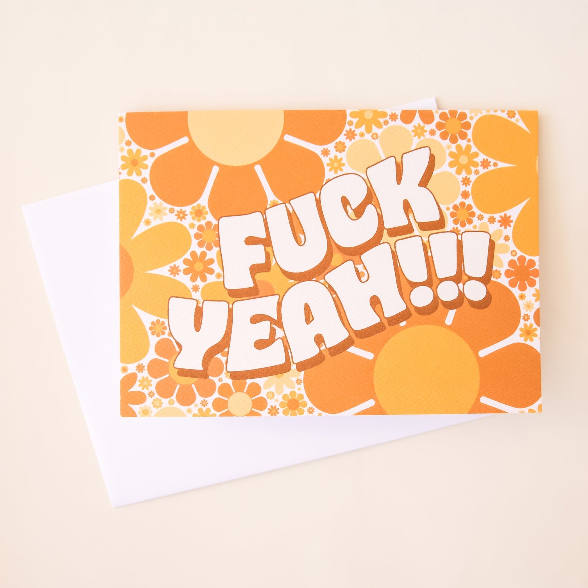 Greeting card filled with retro yellow and orange flowers. The card reads 'fuck yeah!!!' in curved white bubble lettering. The card is accompanied by a solid white envelope.