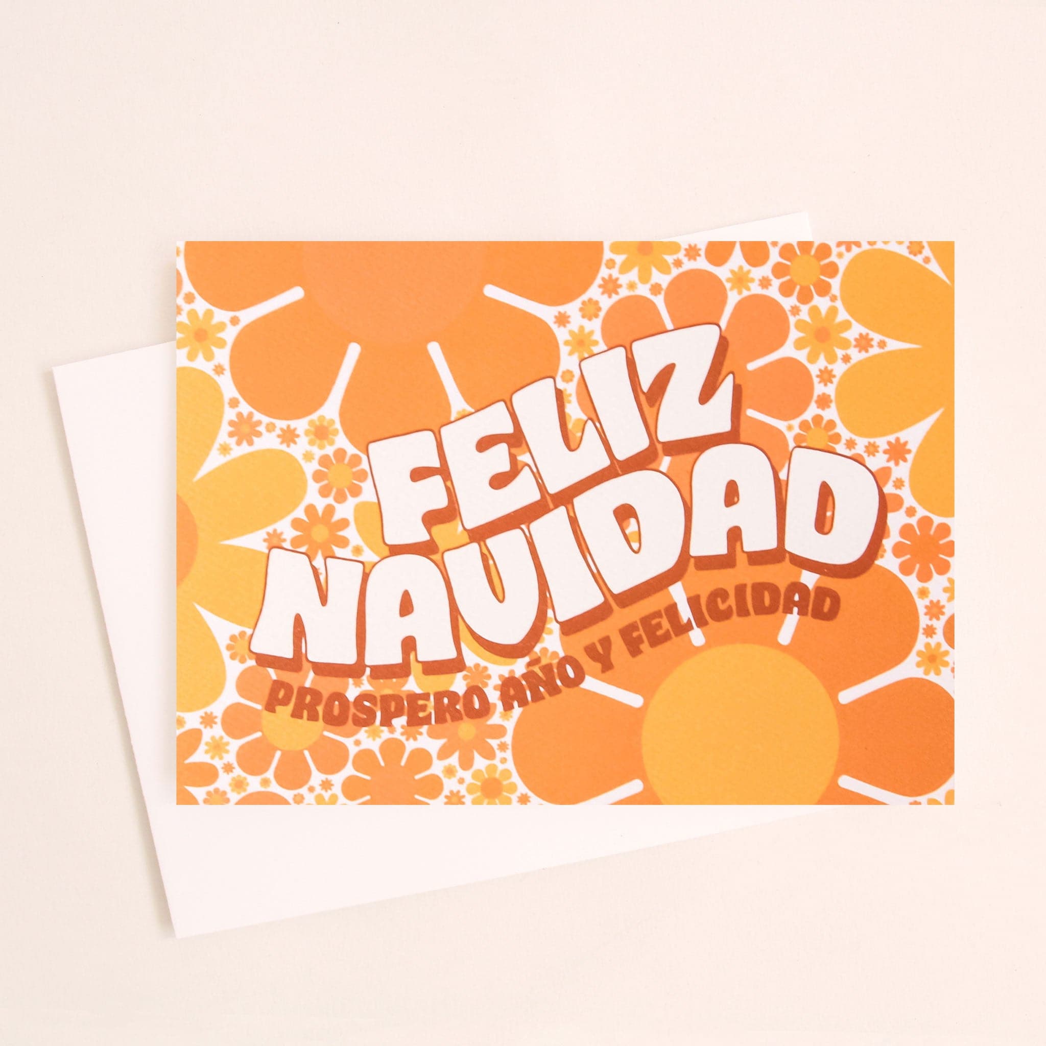 Greeting card filled with yellow and orange retro flower print. The card reads &#39;Feliz Navidad&#39; in white curved bubble letters. Below reads &#39;prosper año y felicidad&#39; in rust colored lettering. The card is accompanied by a solid white envelope. 