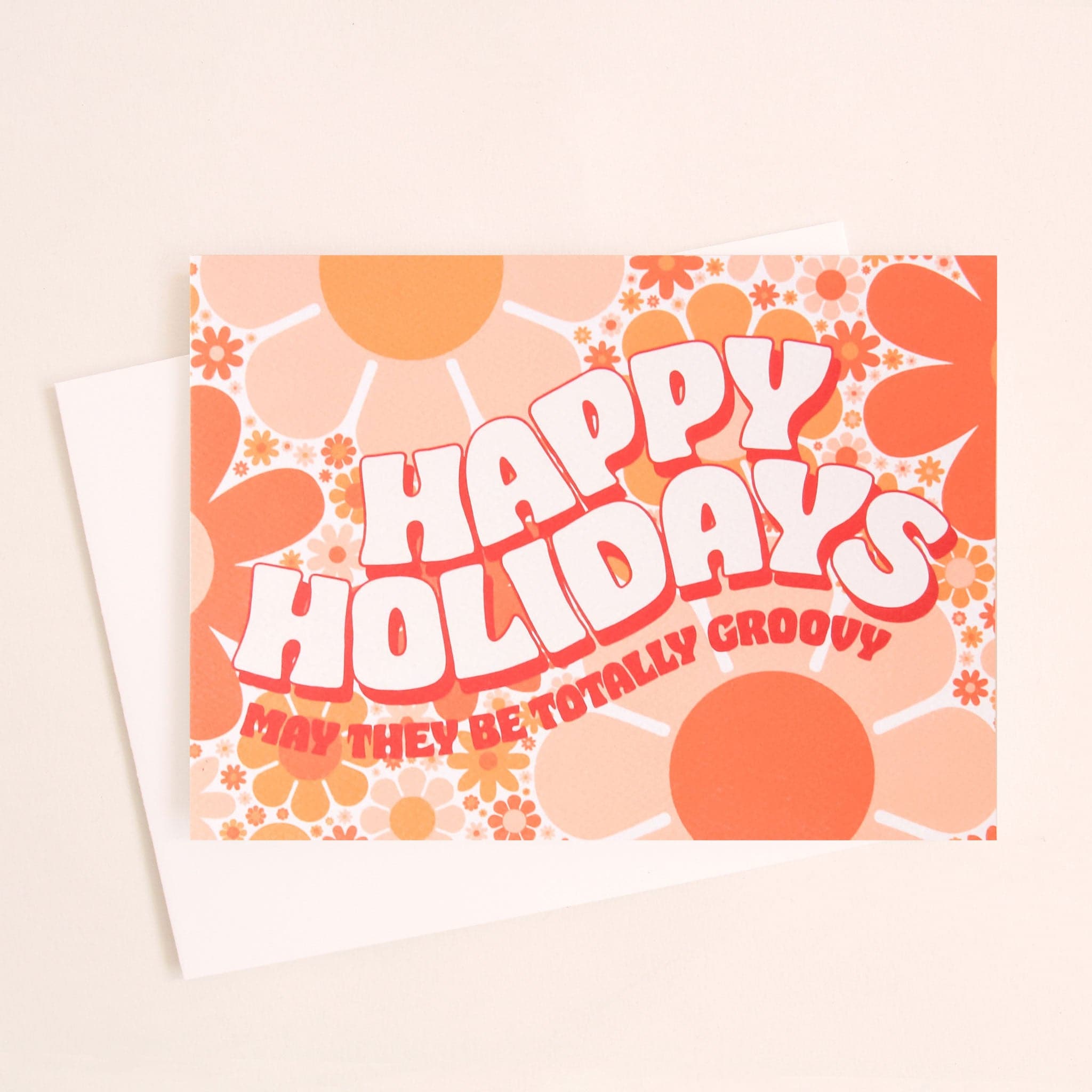Card filled with a funky 70’s design made up of orange and peach daisies. On top of the design is white block lettering with a red shadow that reads ‘Happy Holidays.’ Under that in red block text it reads ‘may they be totally groovy.’ This card is accompanied by a white envelope. 