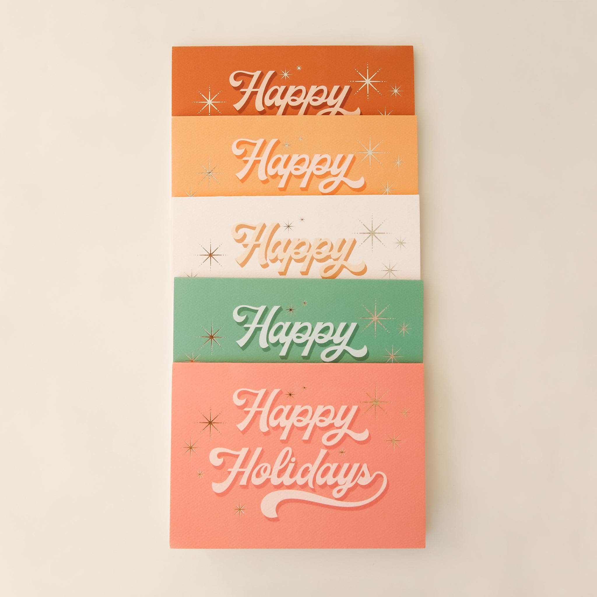 Five pack of holiday cards layered on top of each other in a parallel vertical row. The cards read &#39;happy Holidays&#39; in cursive lettering. 