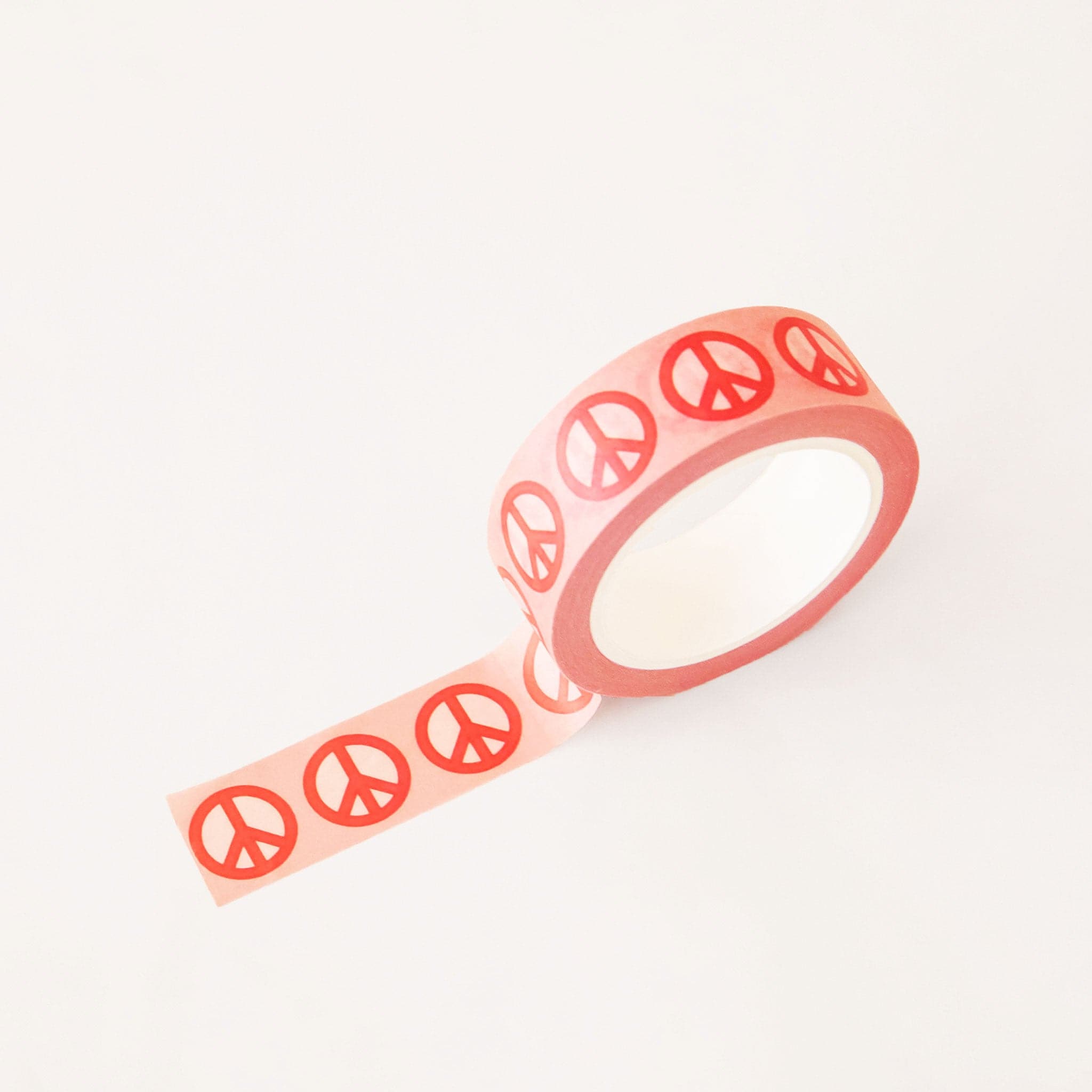 Roll of pink washi tape covered in red classic peace sign symbols. The roll is position upright, partially unrolled.