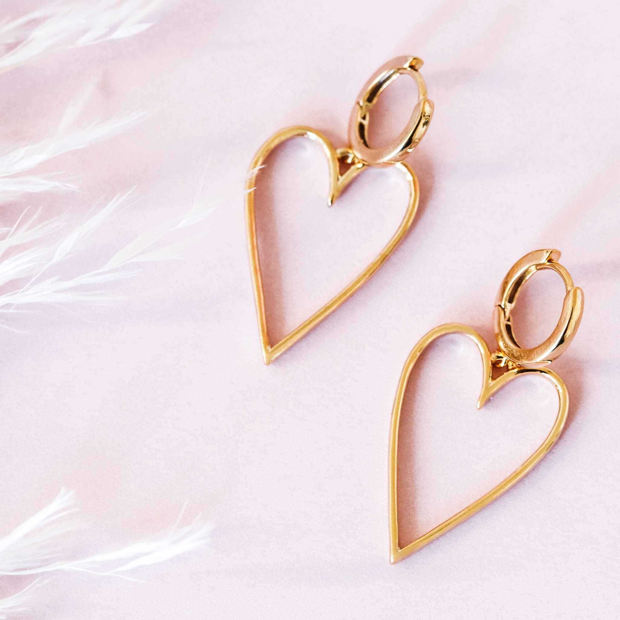 A pair of gold hoop earrings with a larger hold heart shape hoop attached to that.