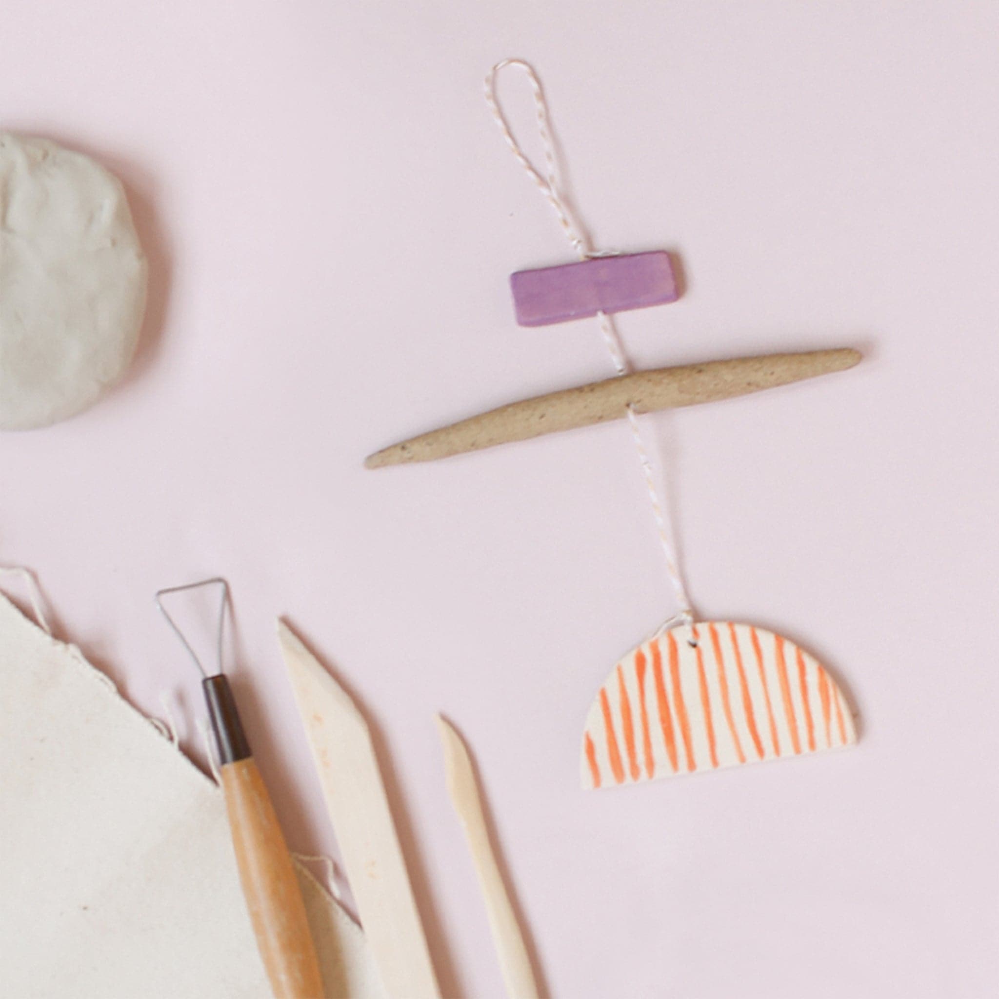 On a light pink background is two clay creations next to a rolling pin and modeling tools.