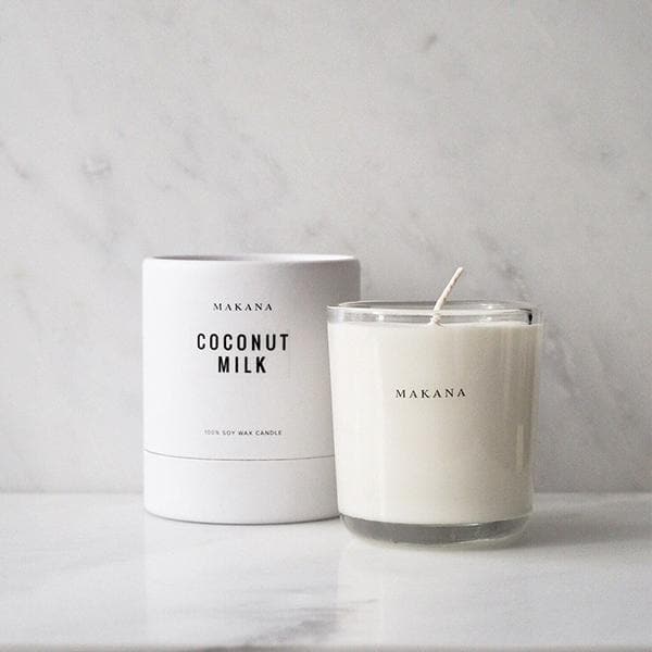 A clear glass jar candle with white wax and a white square label that reads, &quot;Coconut Milk Makana&quot; in clean black text.