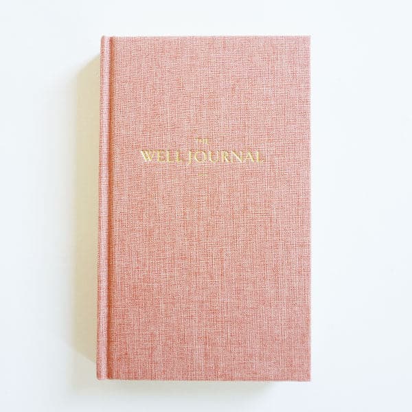 This hardcover journal is titled 'The Well Journal' pressed in gold foil print. The cover itself is a high quality texture covered in warm toned, pink bookcloth. 