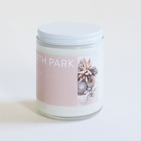 On a white background is a clear glass jar candle with a light pink label on the front that reads, "North Park" along with a white screw on lid.