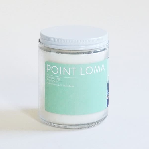 In front of a white background is a clear glass cylinder jar. The jar has a white top. On the front of the jar is a turquoise sticker. On the top of the sticker is white text that reads ‘Point Loma.&#39;