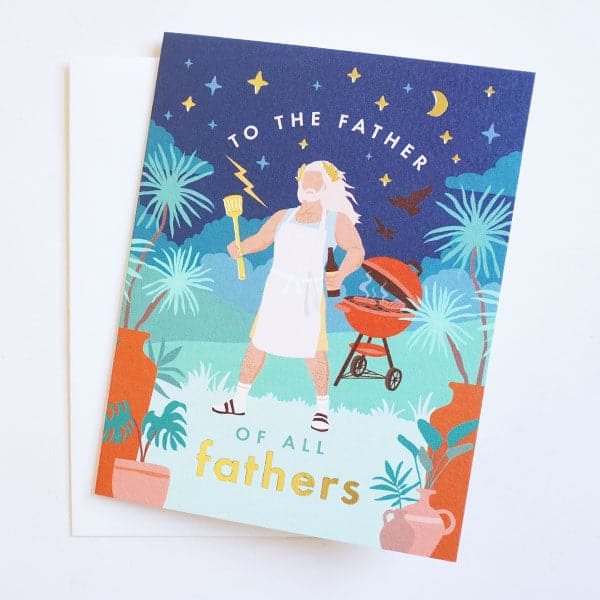 On a cream background is a blue card with a Zeus character illustration holding a grilling tool in his hand along with text that reads, "To The Fathers Of All Fathers". 