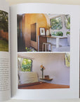 Open page of the book highlighting two tastefully decorated camper interiors. The above interior is wood paneled with open windows and modern white barstools. Below is a peak at a perfectly simple bedroom interior with a burnt orange comforter.