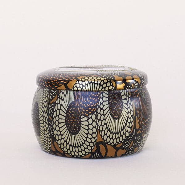 Round tin candle vessel and lid with dark and light gold floral pattern.