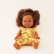 In front of a white background is a baby doll with dark brown curly hair in a yellow dress (not included with purchase). 