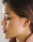A pair of stud earrings featuring a dainty circular pink opal and a smaller Swarovski Crystal accent right above it.