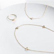 A dainty thin gold band ring with a small gold bee in the center, photographed next to a coordinating bee necklaces.
