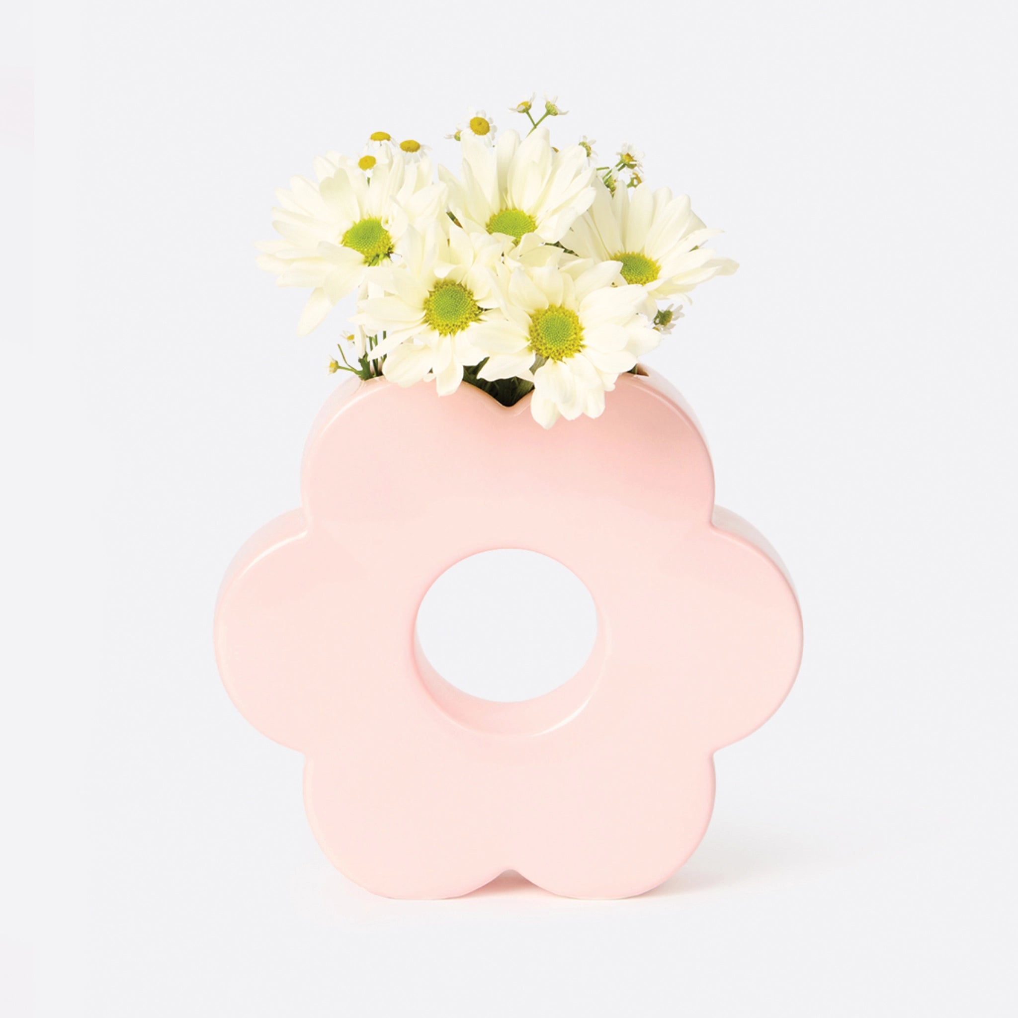 A light pink ceramic vase in the shape of a daisy with an opening in the center and an opening at the top to inset plants and floral stems.