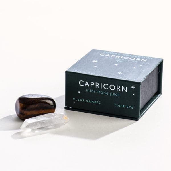 A dark green magnetic box featuring the Capricorn&#39;s mini stone pack. It includes a clear quartz crystal and a tumbled tiger eye stone.