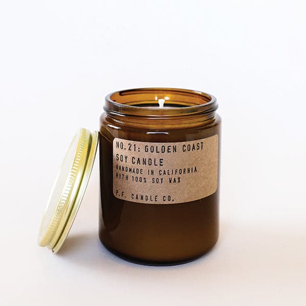 Candle features amber glass with a gold lid. The label is kraft paper with typewriter font that reads "No.21: Golden Coast Soy Candle Handmade in California with 100% Soy Wax. P.F. Candle Co."