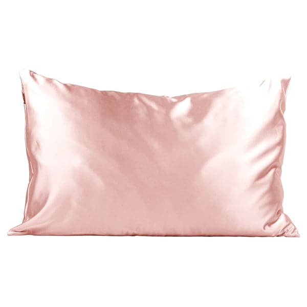 In front of a white background is pillow with a satin pillowcase. The pillowcase is blush pink. 