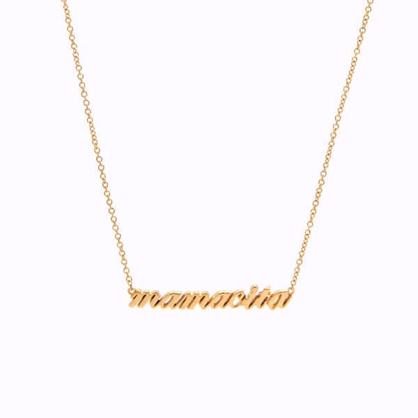 Photo of a gold necklace on a white background. Necklace reads &quot;mamacita&quot; in gold lowercase script. Chain is linked to either side of the word at the top-most point and the chain is leading upwards off the page in a &quot;v&quot; shape.  