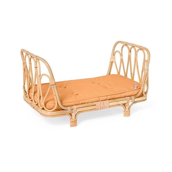 In front of a white background is a light tan wicker day bed. It arches on the right and left side of the day bed. Inside the day bed is an orange mattress.