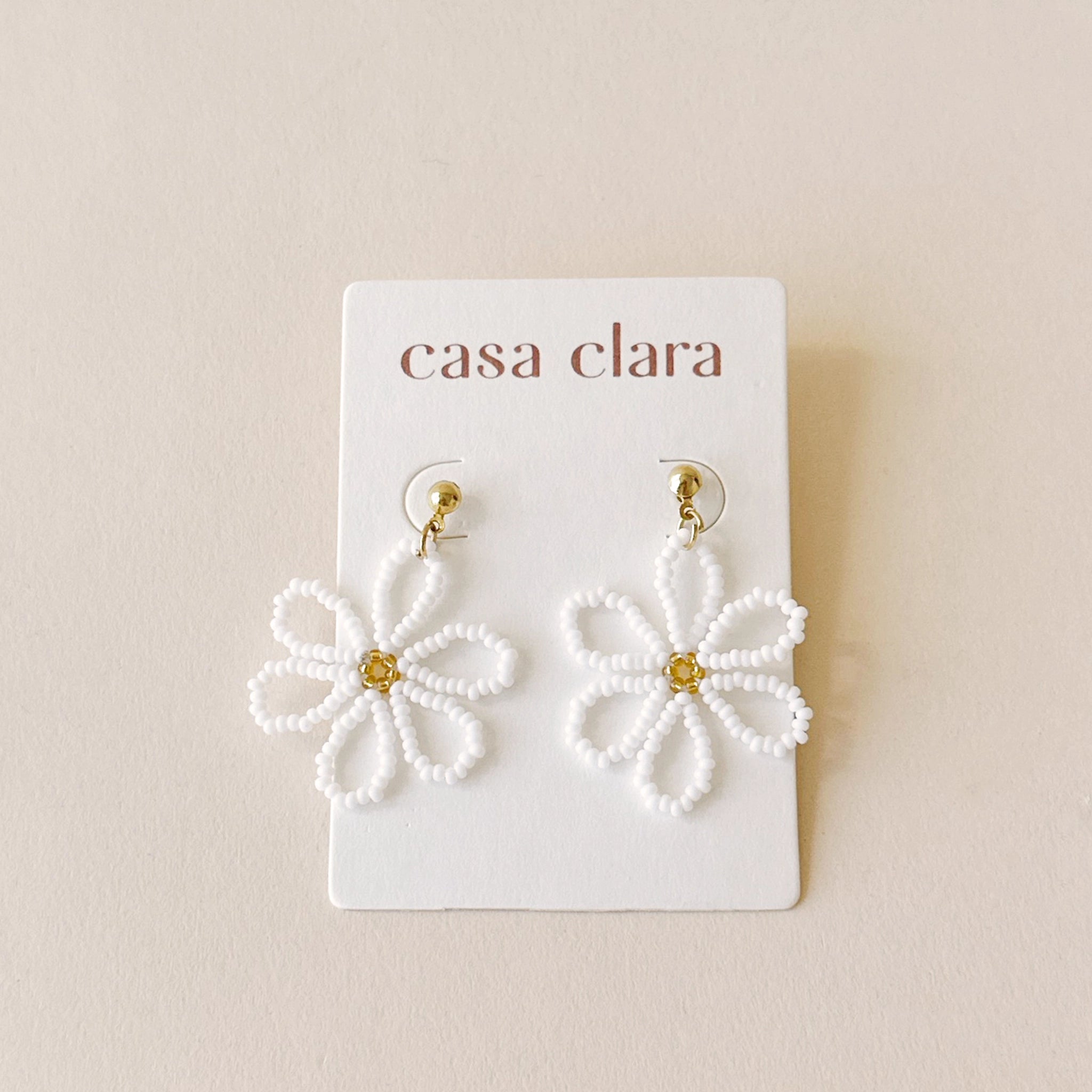 Gold earrings with a white beaded flower dangling from it with a gold beaded center.
