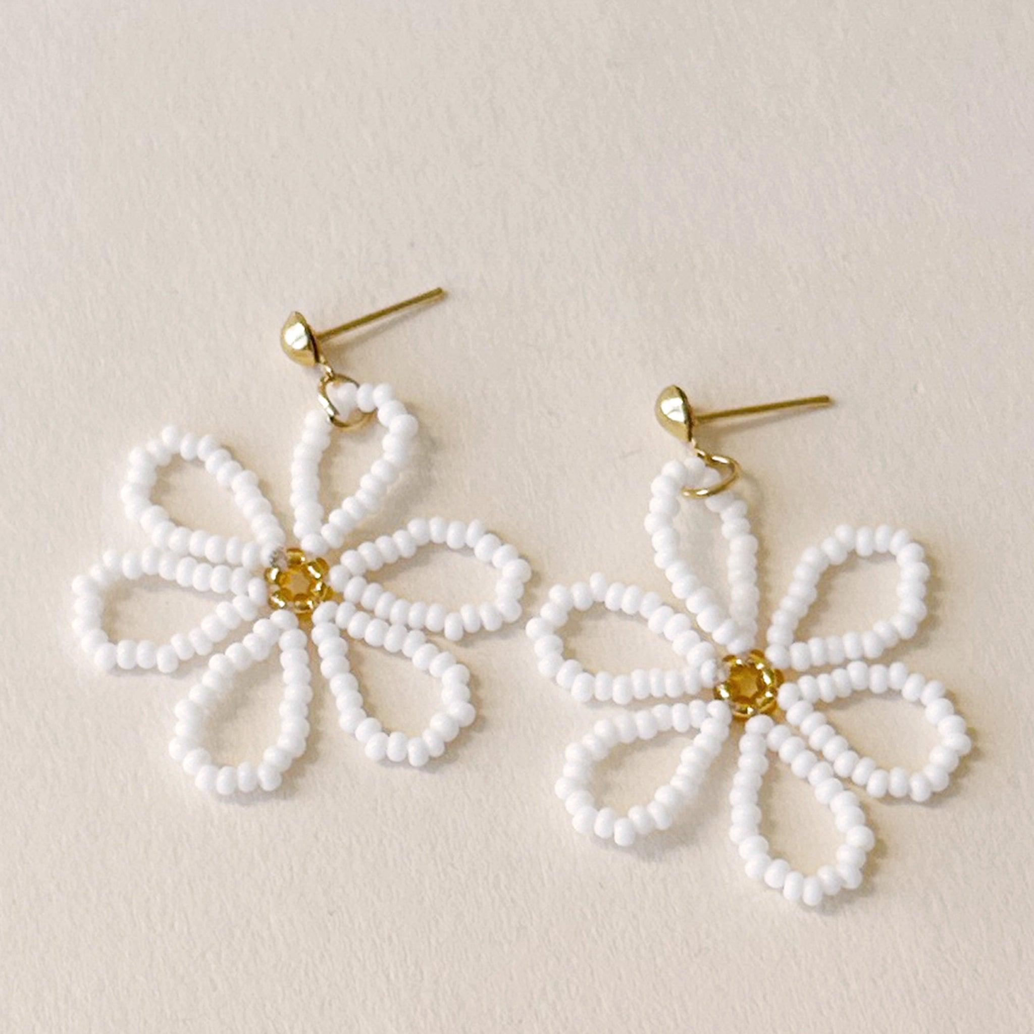 Gold earrings with a white beaded flower dangling from it with a gold beaded center.