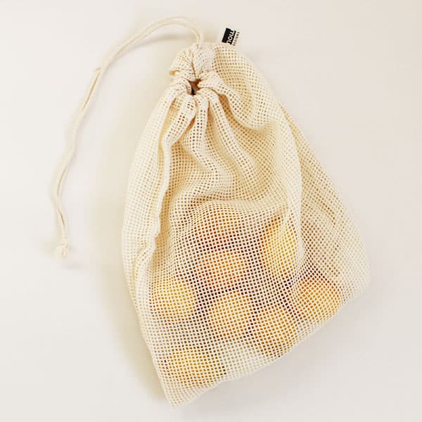 A natural woven produce bag with a cinched tie and a small square hole pattern filled with lemons in this photograph. 